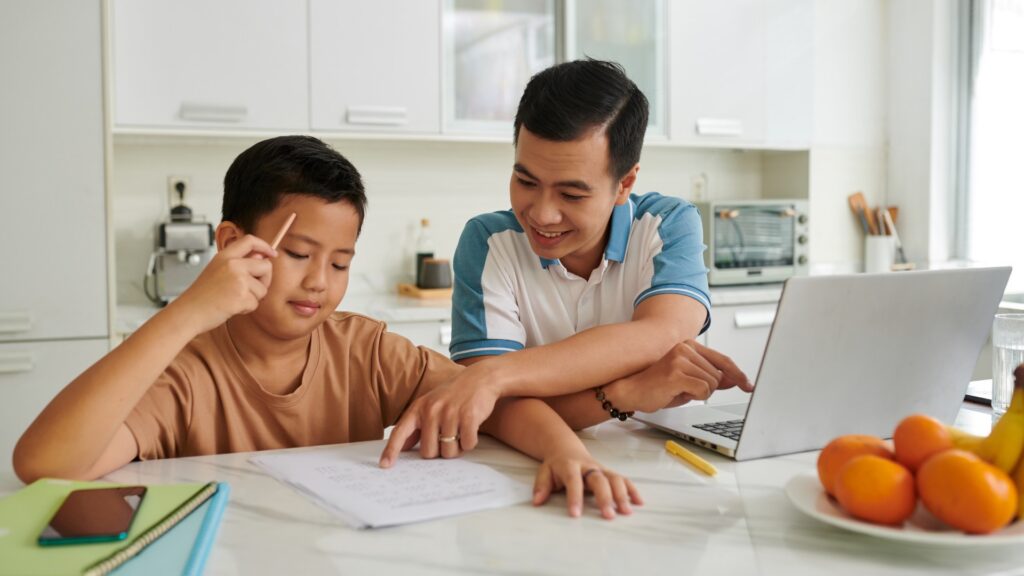 Dad sitting with his son, looking over a math worksheet together